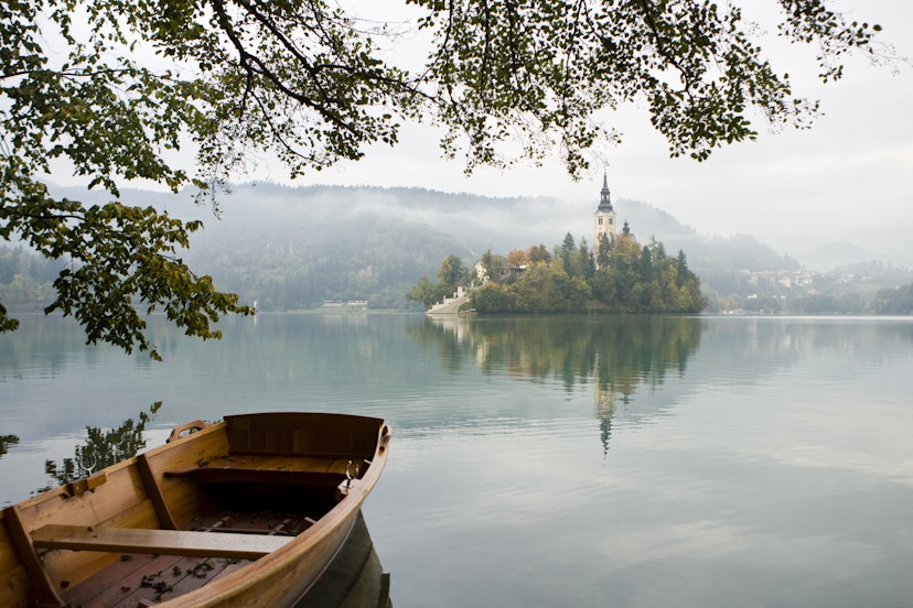 Colorful row boats for touring Lake Bled and beautiful fall colors. Bled Island and Church of Mary the Queen, also known as Church of the Assumption in backdrop.    Bled, Slovenia